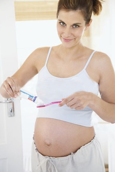 Pregnant woman putting toothpaste on toothbrush